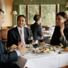 Two businessmen and woman at restaurant table, smiling